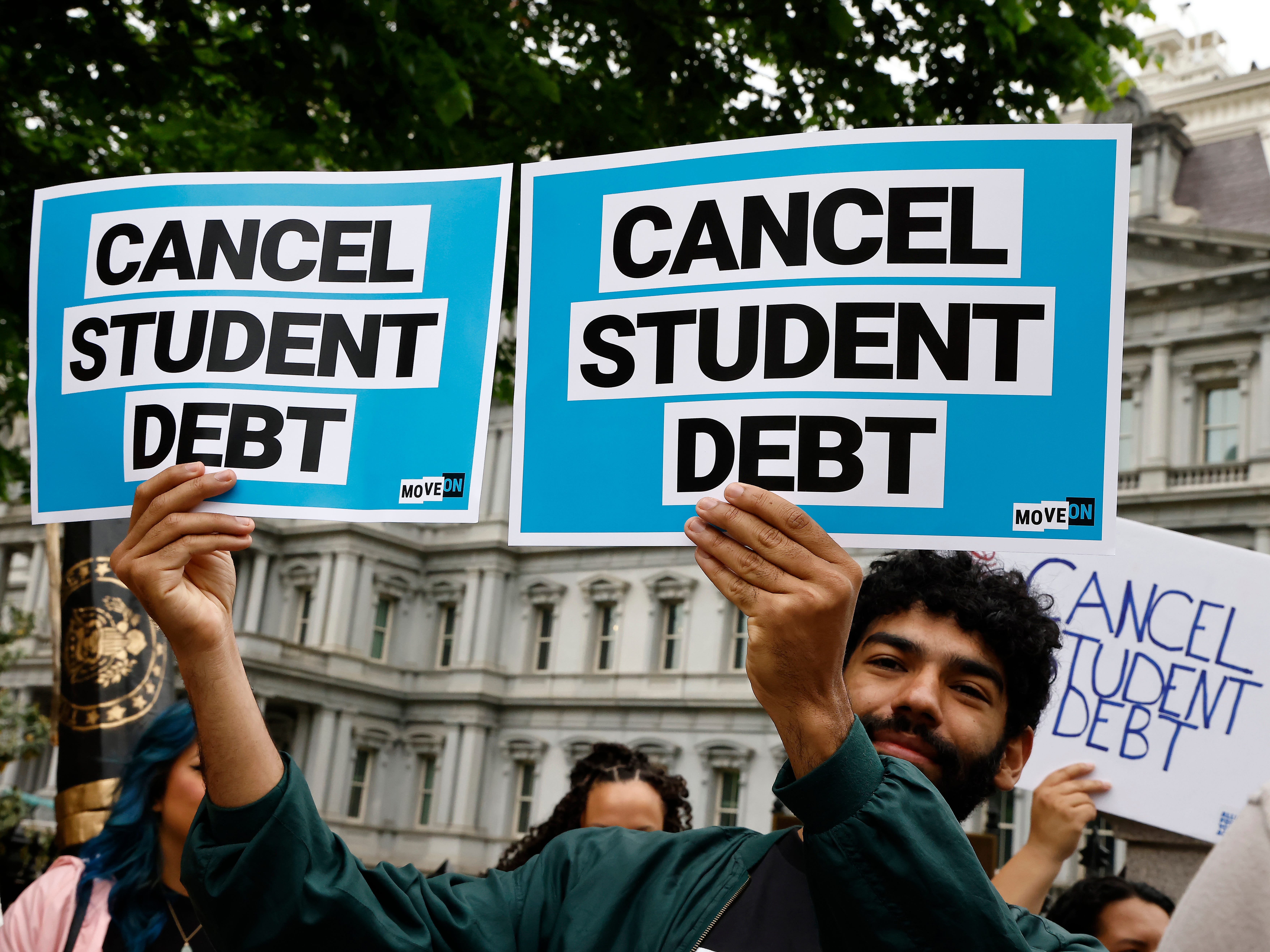 Man holds up two signs that read "CANCEL STUDENT DEBT"